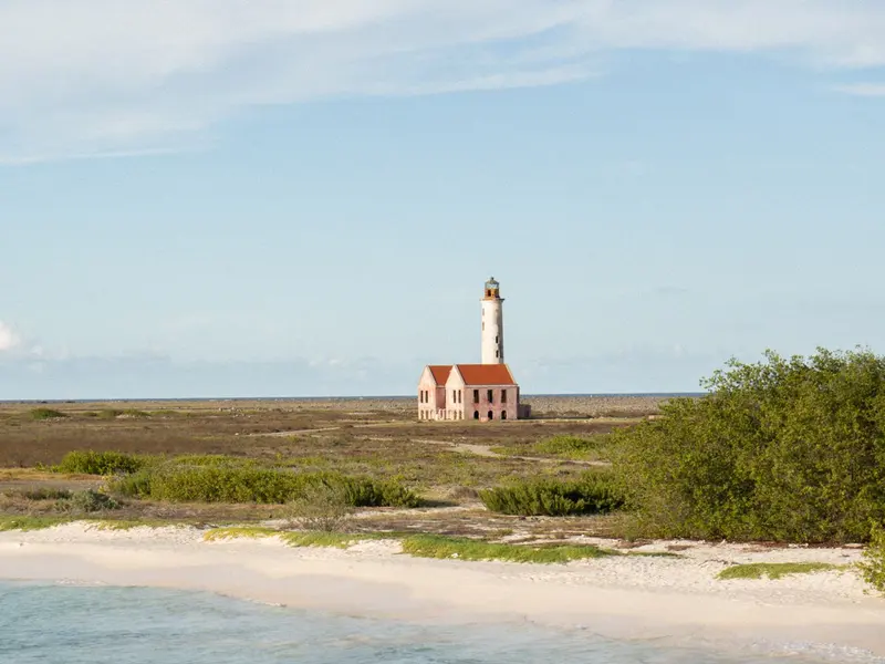 Vuurtoren en roze gebouw op het vlakke eiland Klein Curaçao, met wit zandstrand op de voorgrond